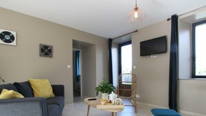 A modern living room with a sofa, a coffee table, a chair, and a TV mounted on the wall. - Comfortable cottage in Saint-Pair-sur-Mer, near Granville beaches (Saint-Pair-sur-Mer)
