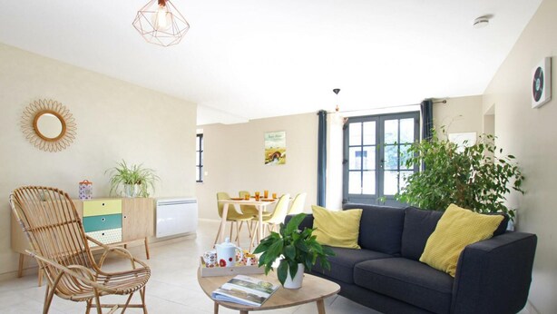 A modern living room with a sofa, a dining table, and a chair. There is a potted plant and a decorative mirror on the wall. - Comfortable cottage in Saint-Pair-sur-Mer, near Granville beaches (Saint-Pair-sur-Mer)