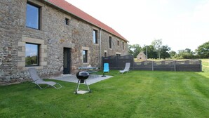 A stone building with a red roof, a grassy yard, and outdoor seating. - Comfortable cottage in Saint-Pair-sur-Mer, near Granville beaches (Saint-Pair-sur-Mer)
