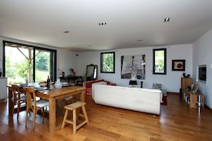 A spacious living area with a wooden dining table, chairs, a sofa, and a TV. - Loft OVEBAS - Domaine de l'Ô  (Saint-Jean-D'eyraud)