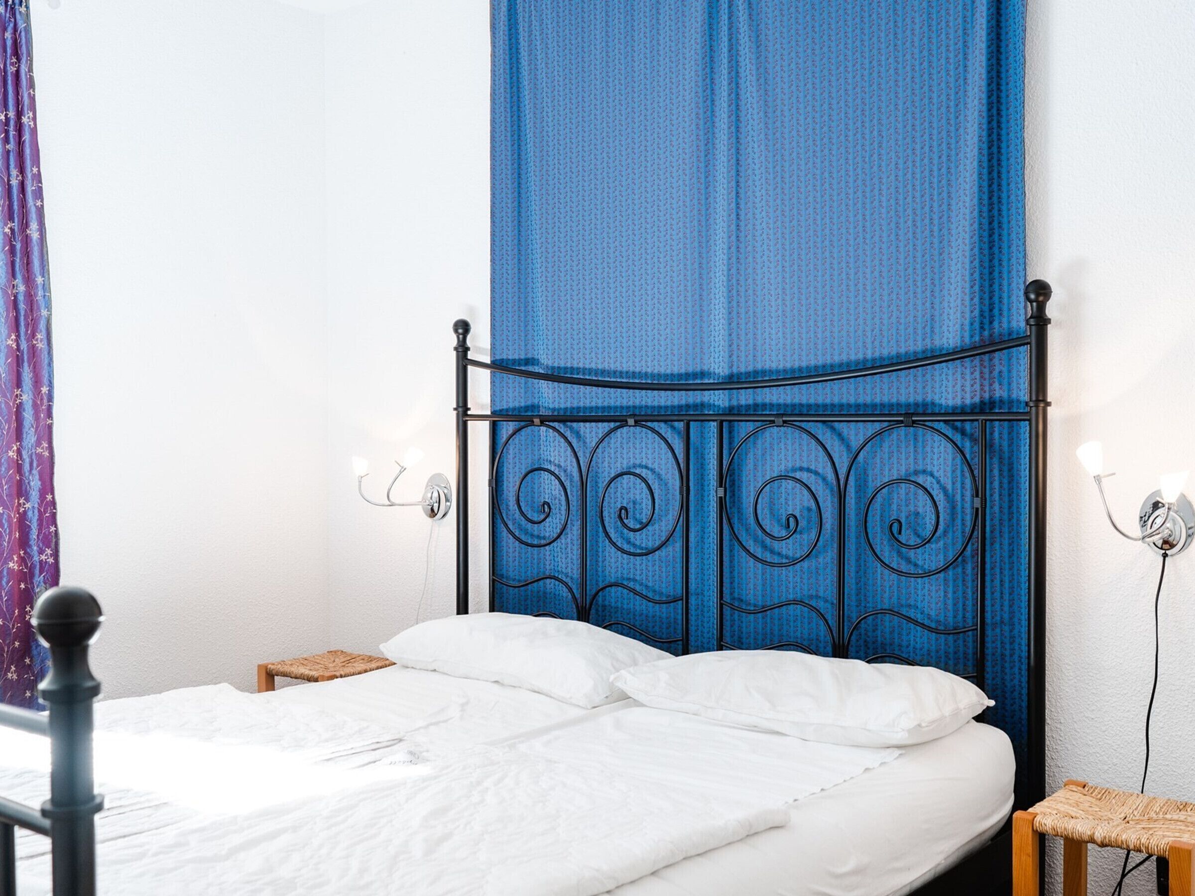A bed with white linens, a metal headboard with a decorative design, and a blue canopy.