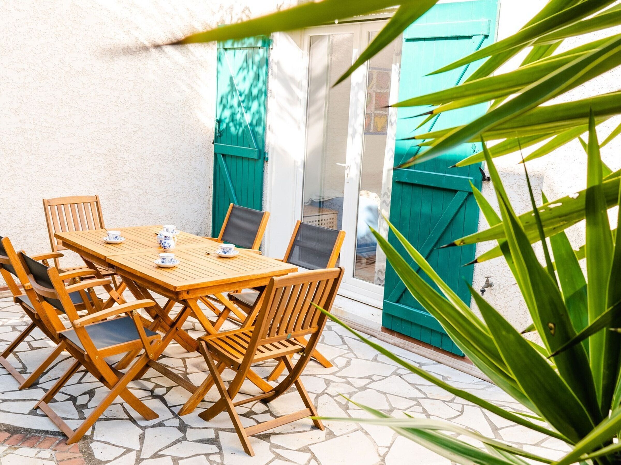 Een houten tafel met stoelen, een betegelde vloer en een groene deur.