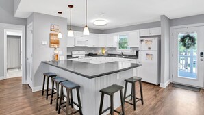 Een moderne keuken met witte kasten, een groot eiland met barkrukken, hanglampen en een koelkast met magneetjes.