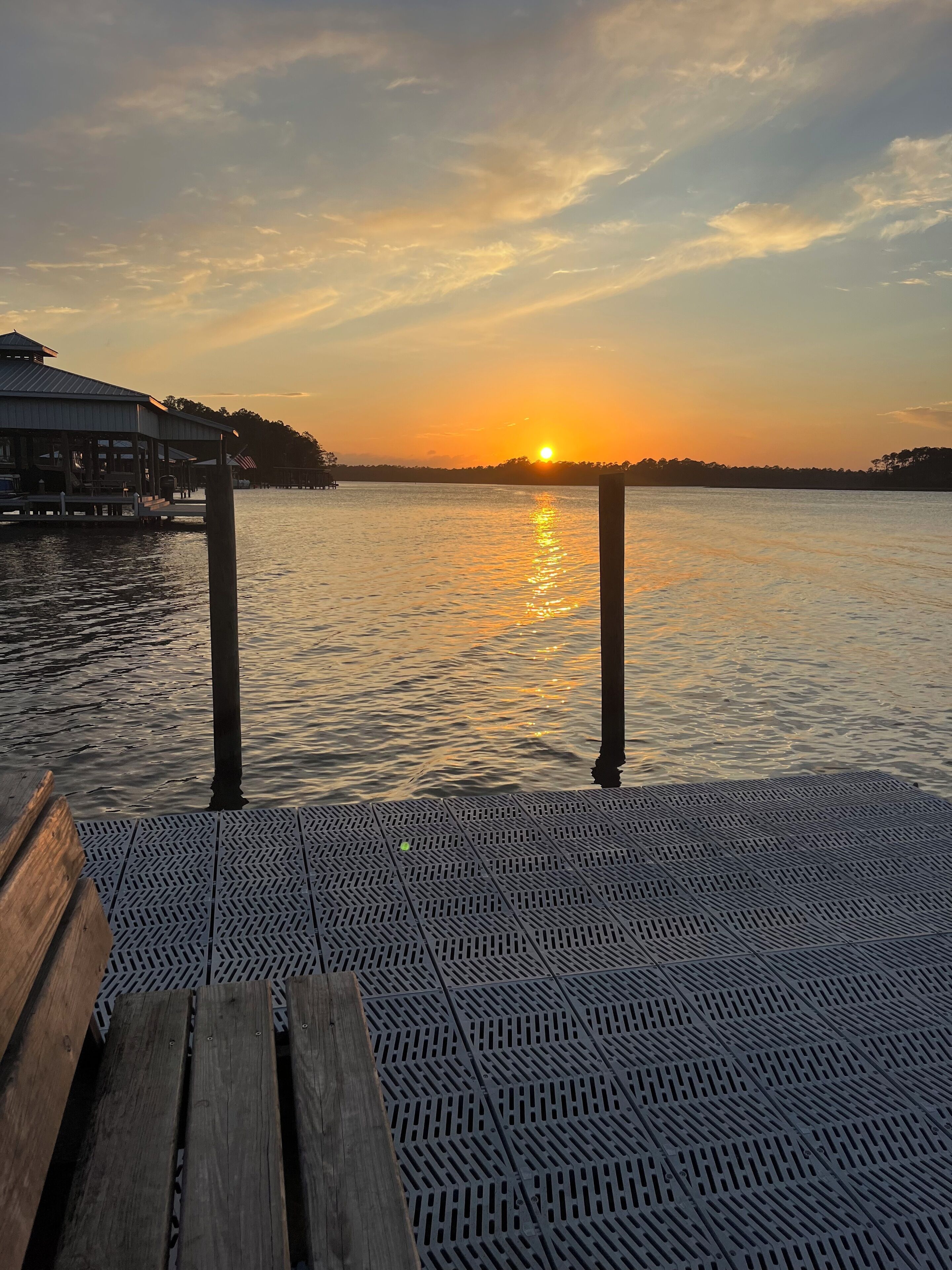 A wooden dock with metal grates leading to a body of water during sunset.