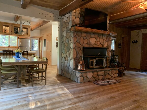 Amplia sala de estar con chimenea de piedra, piso de madera y un comedor con mesa y sillas.