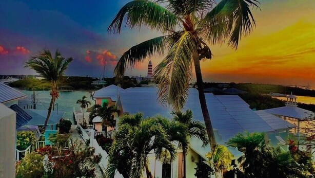 A resort with palm trees, a beach, and a lighthouse in the background.