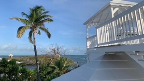 A white building with a balcony overlooking a beach and palm trees.