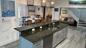A modern kitchen with a central island, pendant lighting, and a dining area with a table and chairs.