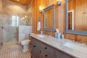 Een moderne badkamer met een glazen douche, twee wasbakken, houten lambrisering en een grote spiegel.
