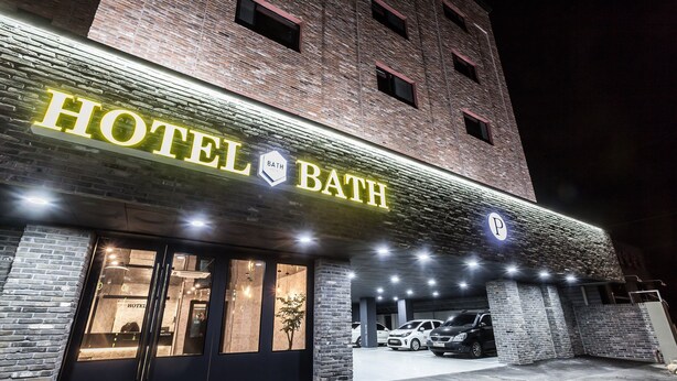 Ein Hotel mit einem auffälligen Schild 'HOTEL BATH', einer Ziegel-Fassade und einem Parkplatz mit Autos.
