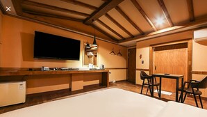 Ein modernes Hotelzimmer mit einem großen Bett, einem Flachbildfernseher, einem Holztisch mit Stuhl und einer kleinen Küchenzeile.