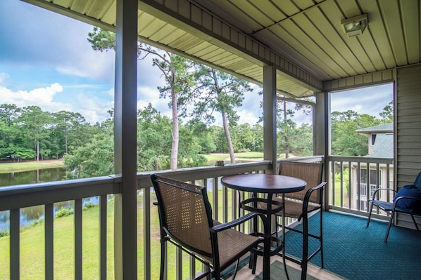 A covered outdoor area with a table and chairs, overlooking a pond and trees.
