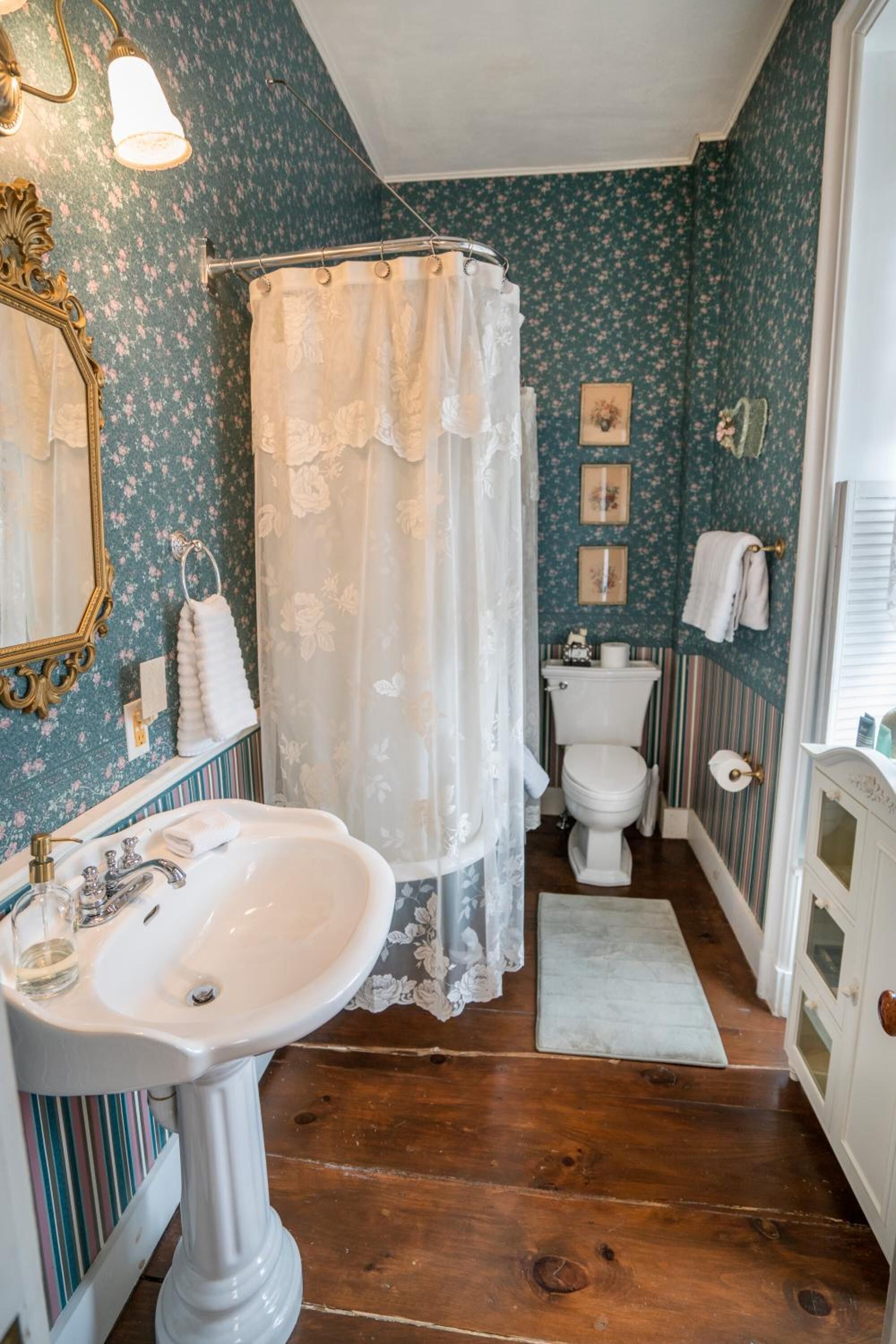 Un baño con lavamanos pedestal blanco, inodoro y ducha con cortina estampada.