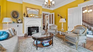 A living room with a fireplace, a chandelier, and a large mirror on the wall.