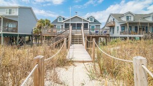 A beachfront property with a wooden boardwalk leading to a house with a balcony and a covered porch.