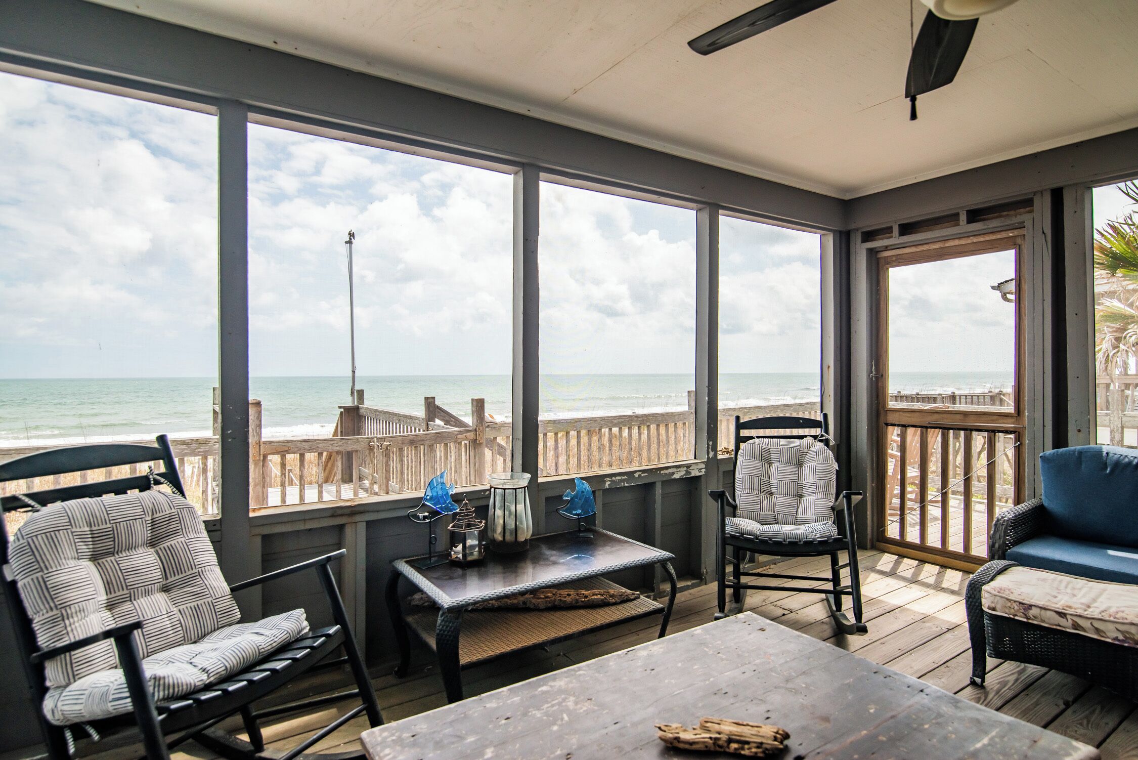 A covered patio with a view of the ocean, featuring a table, chairs, and a wooden deck.