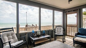 A covered patio with a view of the ocean, featuring a table, chairs, and a wooden deck.