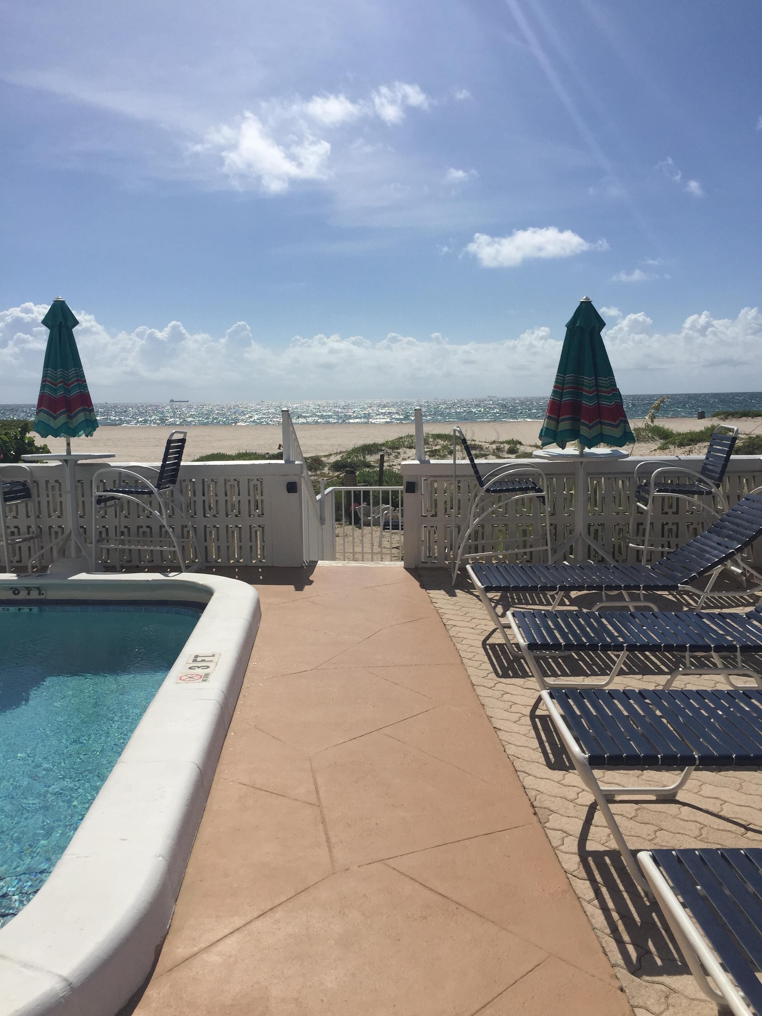 Ein Poolbereich mit Liegestühlen und Sonnenschirmen, mit Blick auf einen Strand.