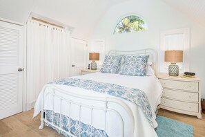 Een slaapkamer met een bed, twee nachtkastjes, een dressoir, een raam met uitzicht en een deur.