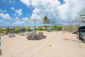 A beachside patio with outdoor seating, including chairs and tables, under umbrellas, and a view of the ocean.