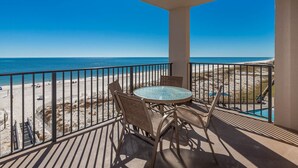 Un balcon avec vue sur la plage, une table ronde avec des chaises et un espace piscine.