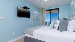 Une chambre à coucher comprenant un lit, un téléviseur à écran plat fixé au mur, une fenêtre avec vue et une porte donnant sur un balcon extérieur.