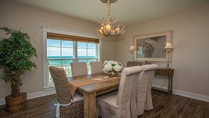 A dining area with a wooden table, wicker chairs, a chandelier, a view of the ocean, and a framed picture on the wall. - North end of Cape Gulf Front 1 level w/elevator from carport & screened-in porch (Cape San Blas)