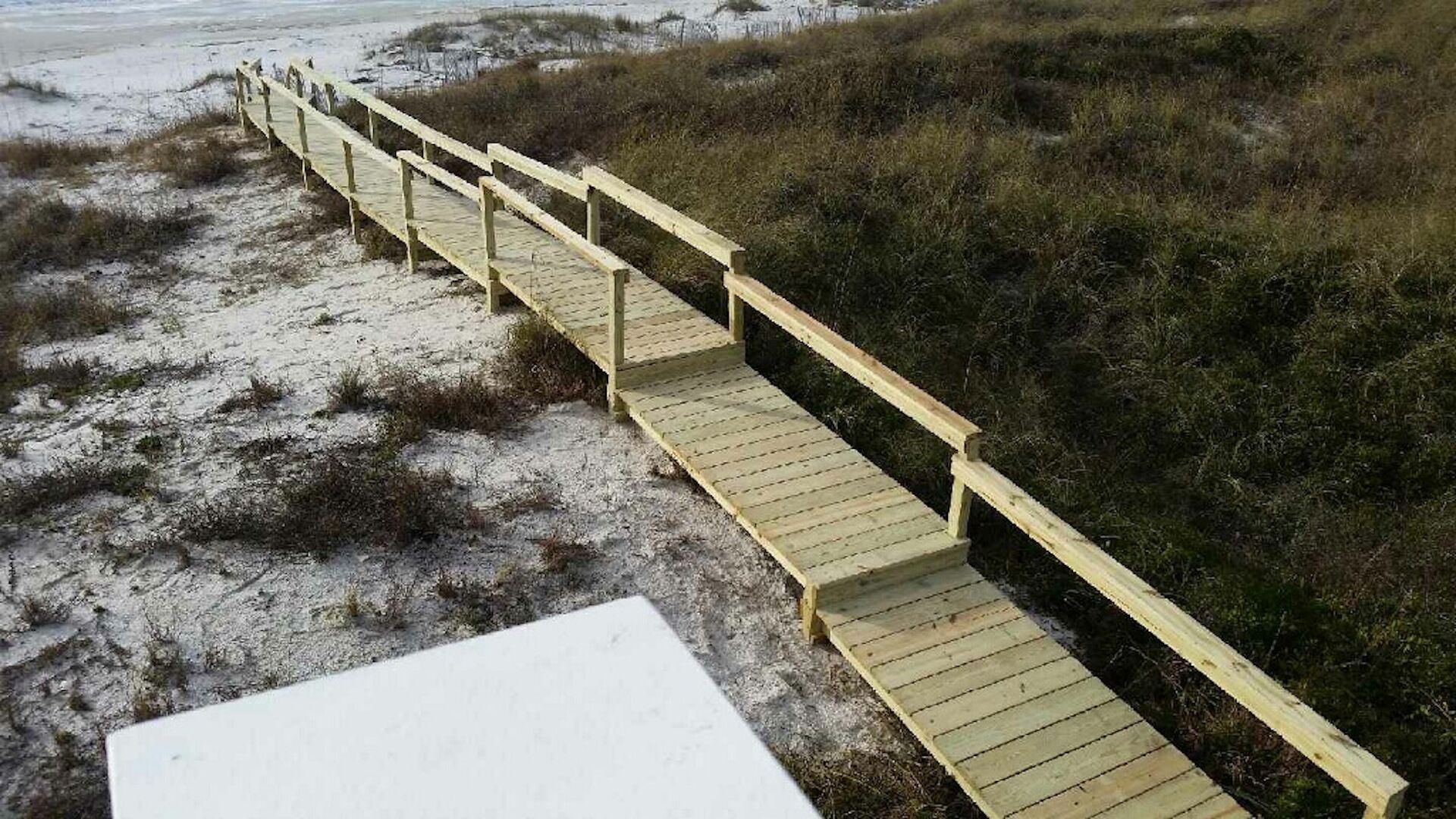 A wooden boardwalk leading through a sandy area with grass.