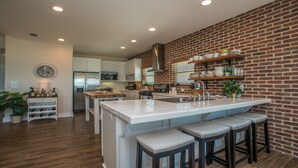 A modern kitchen with a central island, bar stools, and a brick accent wall. - North end of Cape Gulf Front 1 level w/elevator from carport & screened-in porch (Cape San Blas)