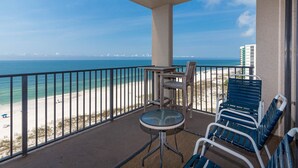 A balcony with a view of the beach and ocean, featuring a table and chairs.