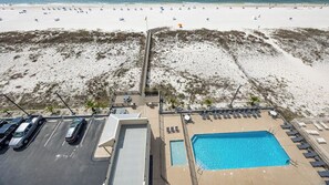Vista aérea de um hotel à beira-mar, com piscina, cadeiras de praia e estacionamento.