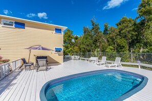 Une piscine avec une terrasse en bois, des chaises longues et un espace salon abrité.
