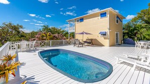 Un área junto a la piscina con piscina, terraza blanca y mobiliario de exterior.