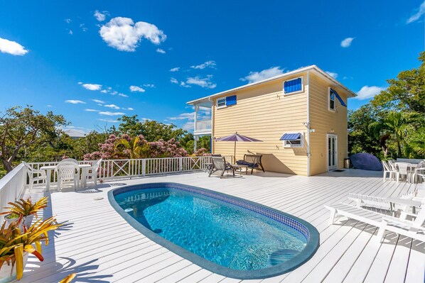 Un espace aménagé au bord de la piscine, comprenant une piscine, une terrasse blanche et du mobilier d’extérieur.