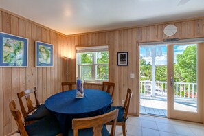 Un coin repas avec une table ronde, des chaises en bois et une vue sur l’extérieur grâce à de grandes fenêtres.