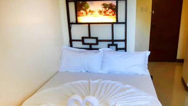 A neatly made bed with white linens and a towel arrangement in the shape of swans. - Bakasyunan Inn Laoag (Laoag)