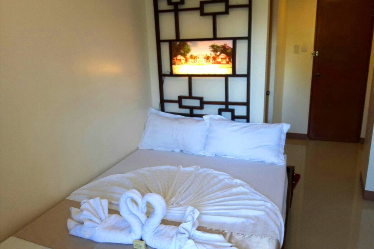 A hotel room with a bed, white pillows, a decorative wall panel, and a door.