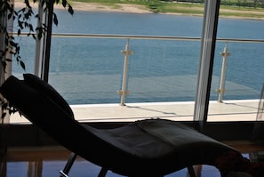 Une pièce avec vue sur un lac, un fauteuil et une rambarde.
