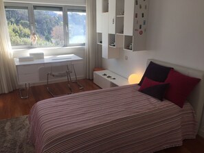 Une chambre à coucher avec un lit, un bureau, une chaise et une vue sur un lac, visible par la fenêtre.