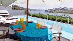 Un espace repas aménagé au bord de la piscine, avec une table dressée pour deux personnes, offrant une vue panoramique sur un lac et des collines.