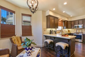 A modern kitchen with dark wood cabinets, a central island with stools, and a dining area with wicker furniture. - Ocean-View Endless Summer Condo with AC & EV Charger (Pismo Beach)