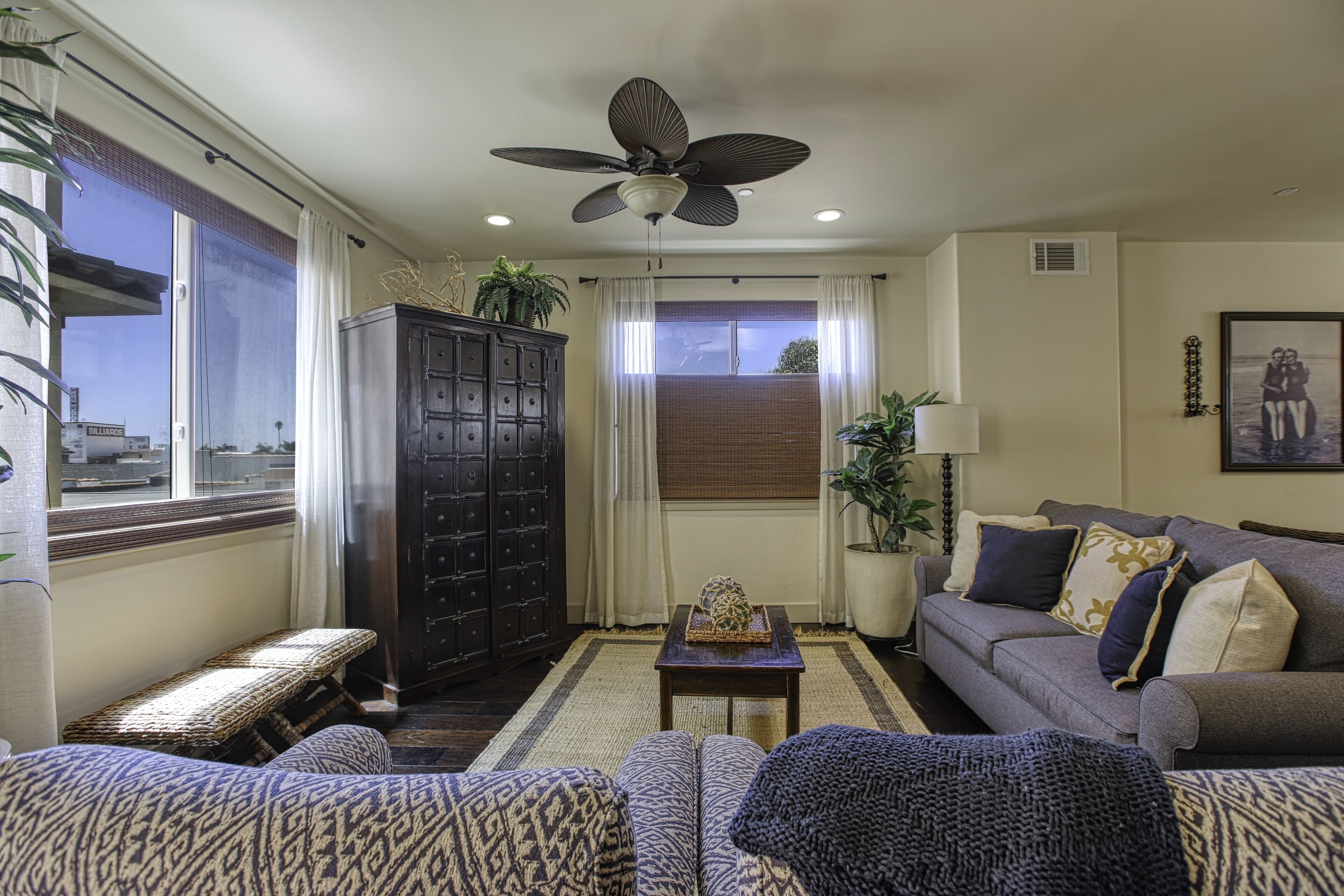 A living room with a sofa, a bench, a cabinet, a ceiling fan, and a window with curtains.