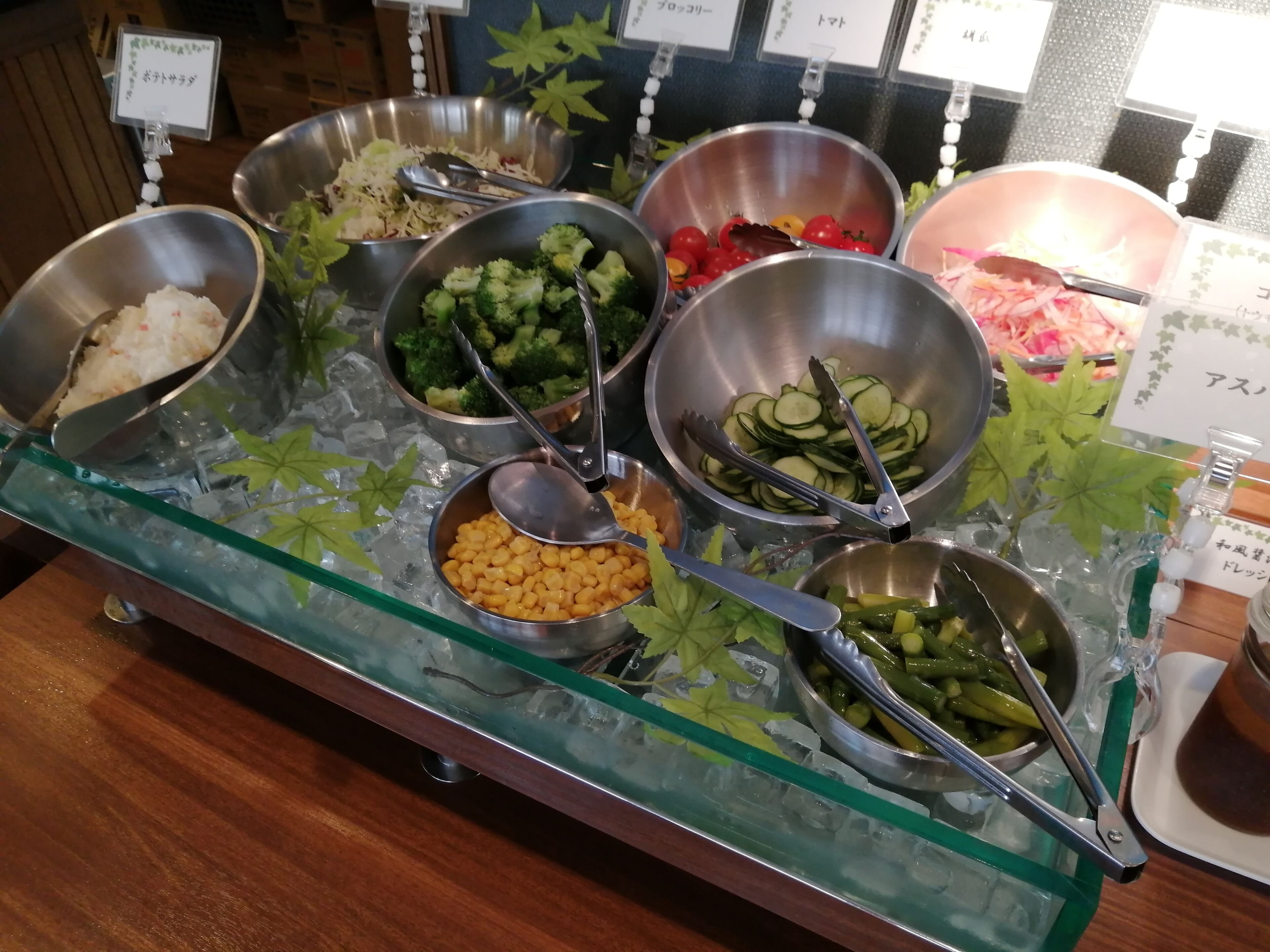 Un bufé con diversos alimentos en recipientes de metal sobre una mesa de vidrio con hielo.