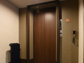 A hotel room with a wooden door, a wall-mounted phone, and a luggage cart. - RHotels Inn Hokkaido Asahikawa (Asahikawa)