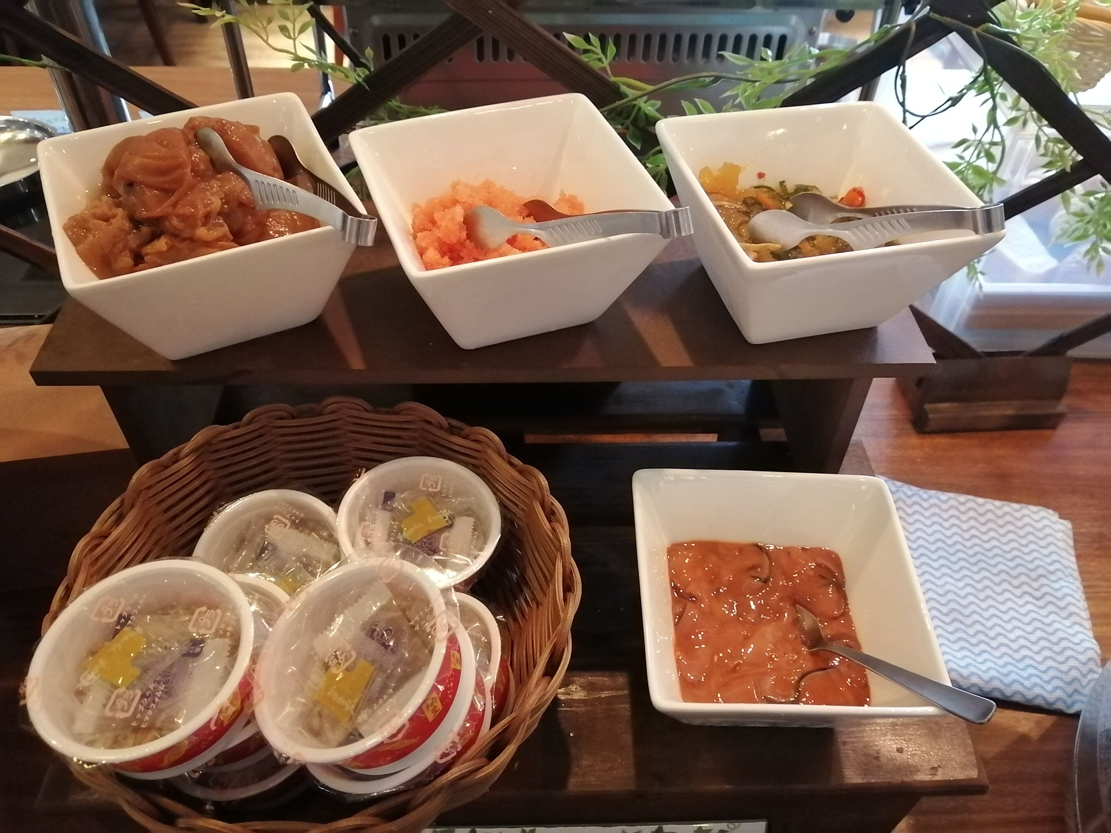 A table with three bowls of food, a basket with cups, and a bowl of soup.