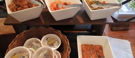 A table with three bowls of food, a basket with cups, and a bowl of soup.