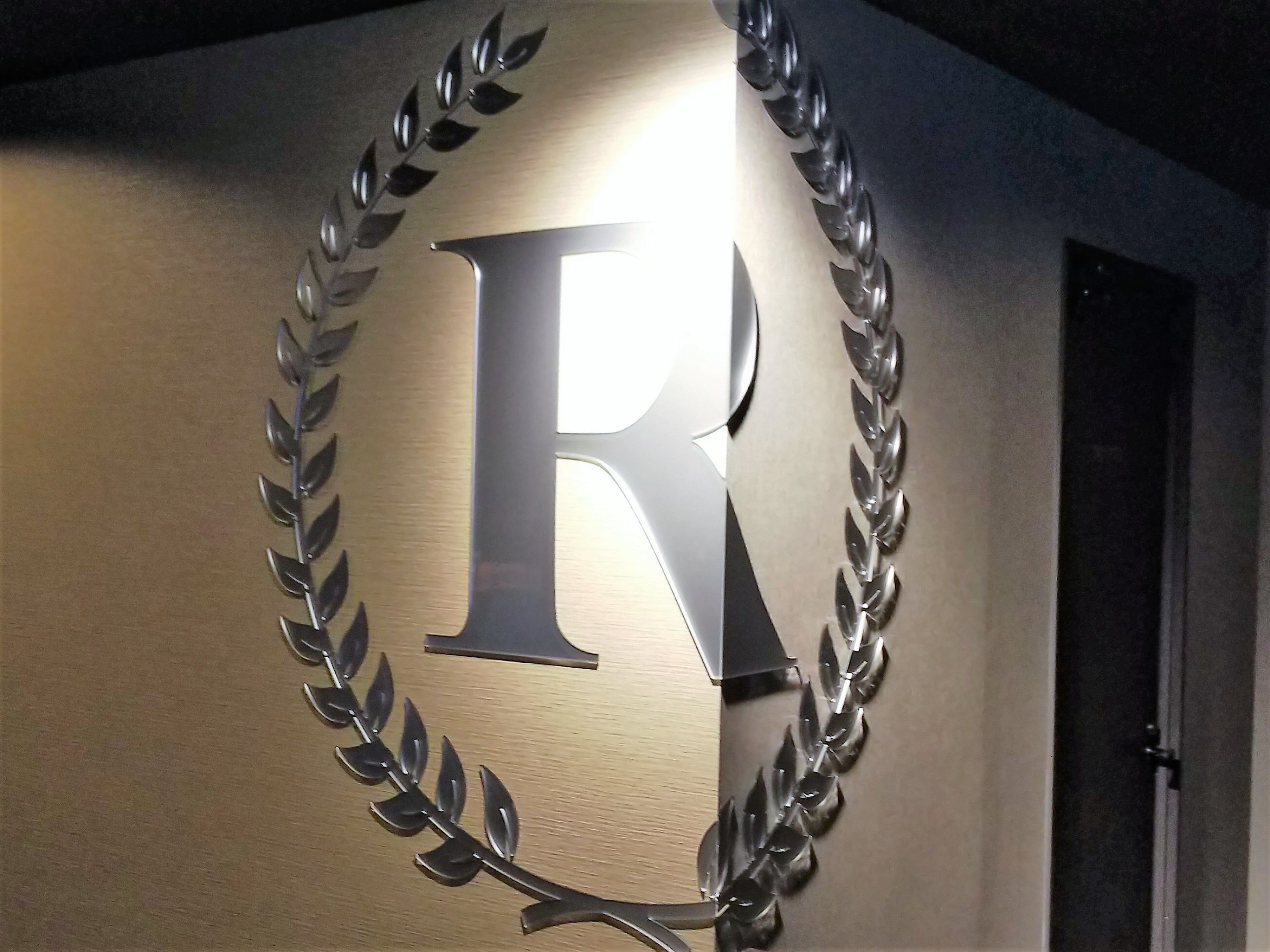 Un letrero en la pared con una letra 'R' grande rodeada de hojas de laurel.