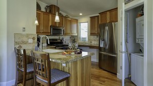 A kitchen with wooden cabinets, stainless steel appliances, a granite countertop, and a dining area with chairs. - Studio condo with ocean views, steps to the beach (Avila Beach)
