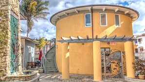 A building with a curved yellow facade, a stone exterior on one side, and a staircase leading to an entrance. - Studio condo with ocean views, steps to the beach (Avila Beach)