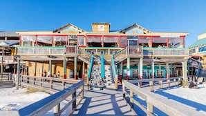 Une jetée mène à un bâtiment à plusieurs niveaux, doté d’espaces de détente en plein air et d’une enseigne indiquant « Café froid ».
